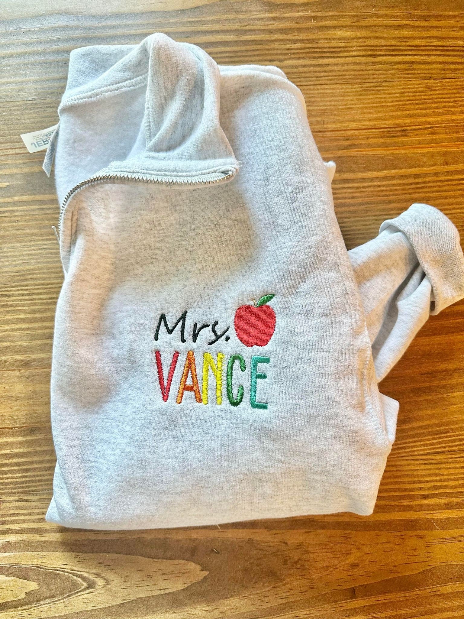 Personalized Teacher Name Quarter Zip Sweater Shown in Ash Color - Teachers name is Embroidered in Rainbow with an apple - Flatlay